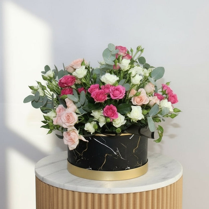 Bouquet of pink and white flowers in a black container on a light gray background