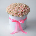 White box with pink roses and a pink ribbon on a wooden surface.