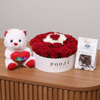 White teddy bear with a red heart, box of red roses, and a card on a wooden surface.