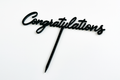 An elegant black acrylic "Congratulations" cake topper with a long stick for inserting into a cake