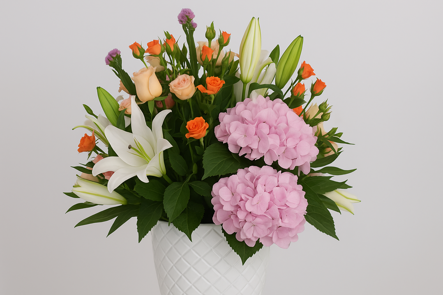Bouquet of flowers with pink hydrangeas, white lilies, and orange roses in a white vase on a light gray background.