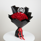 Bouquet of red roses wrapped in black paper with a 'Happy Birthday' card on a white surface.