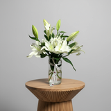 Elegant white lilies bouquet in a glass vase with green leaves and decorative ribbon
