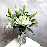 Elegant white lilies bouquet in a glass vase by Pooji Flowers with a decorative ribbon