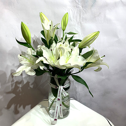 Elegant white lilies bouquet in a glass vase by Pooji Flowers with a decorative ribbon