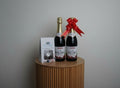 Two bottles of Night Orientale wine with a red bow, a box, and a glass on a white surface.