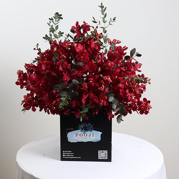 A bouquet of red flowers with green leaves, arranged in a black box with a label that says 'Pooji'.