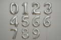 Silver helium balloons in the shape of numbers 0 through 9 in a square format
